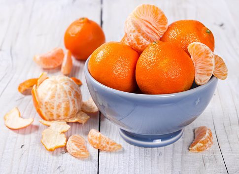 Fresh tangerines in a ceramic bowl on a wooden background