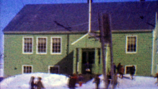 1957: One room schoolhouse kids play outside winter cold sunny day.
