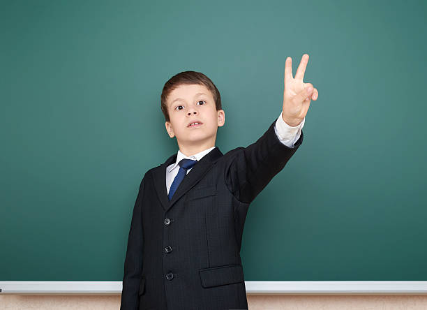istock school boy in black suit show two finger gesture 533974468