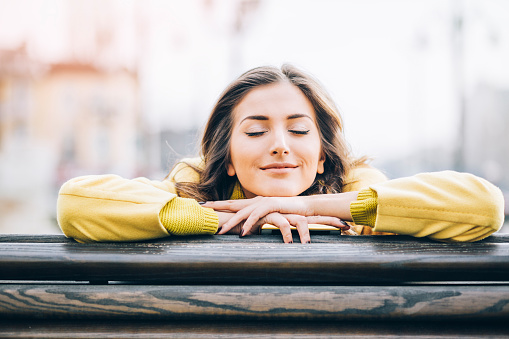 Beautiful young woman sitting on a bench enjoying the sunlight outdoors in the city, with copy space