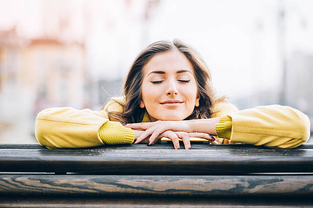 Daydreaming and enjoying the sunlight Beautiful young woman sitting on a bench enjoying the sunlight outdoors in the city, with copy space dreaming stock pictures, royalty-free photos & images