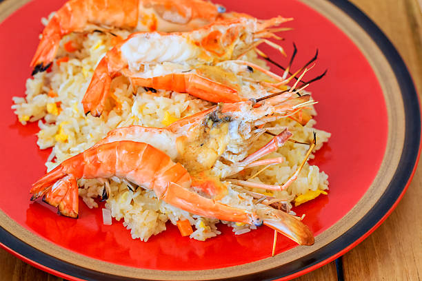 Chef's hands holding a large traditional paella pan filled with saffron rice, shrimp, mussels, and vegetables