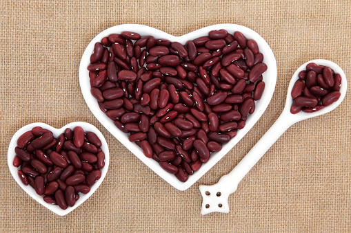 Kidney beans in heart shaped porcelain dishes and spoon forming an abstract background over hessian.