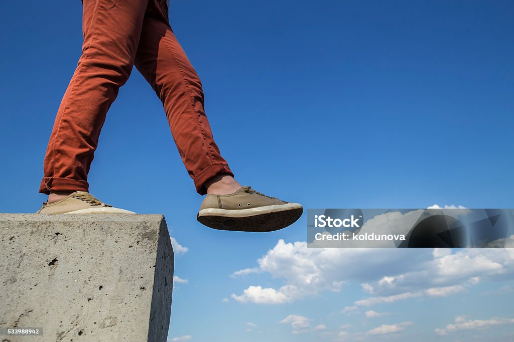 person makes confident step with concrete wall person makes confident step with concrete wall on the white fluffy clouds in blue sky, sunny spring day Activity Stock Photo