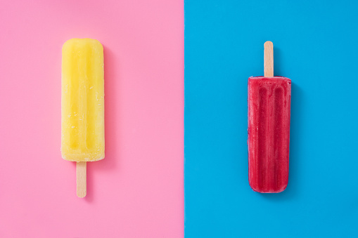 Strawberry popsicle and lemon popsicle on pink and blue background