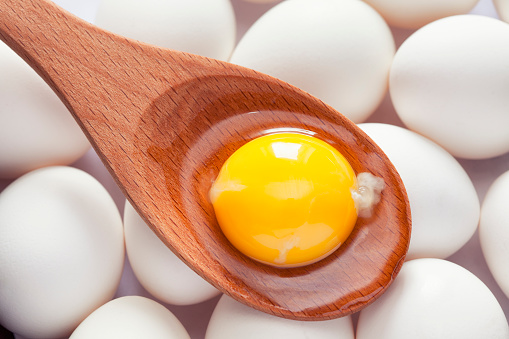 Egg yolk in wooden spoon on eggs. Close up.