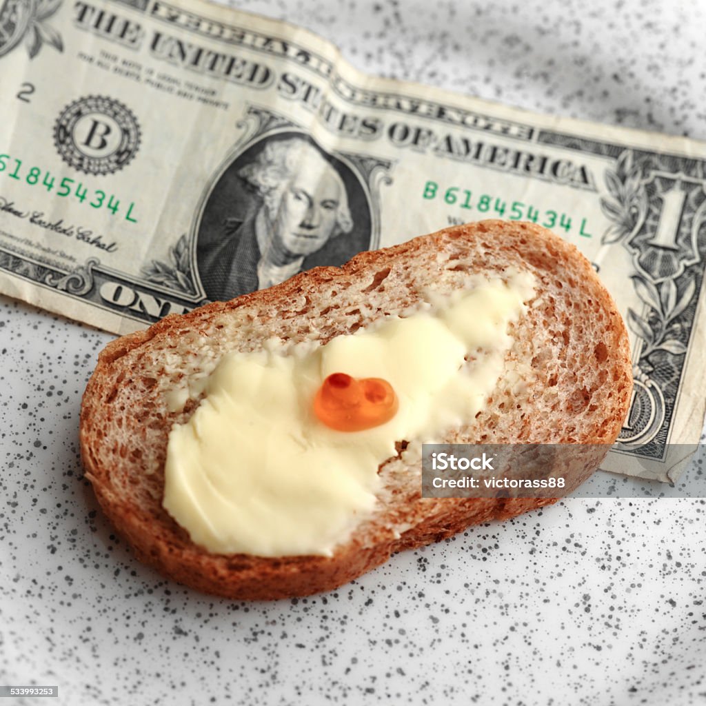Dollar and Caviar Close up overhead shot of pitiful amount of red caviar on a top of bread with butter, dollar banknote in the background 2015 Stock Photo
