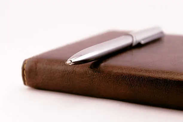 Close-up view of an agenda with leather covers and a silver pen.