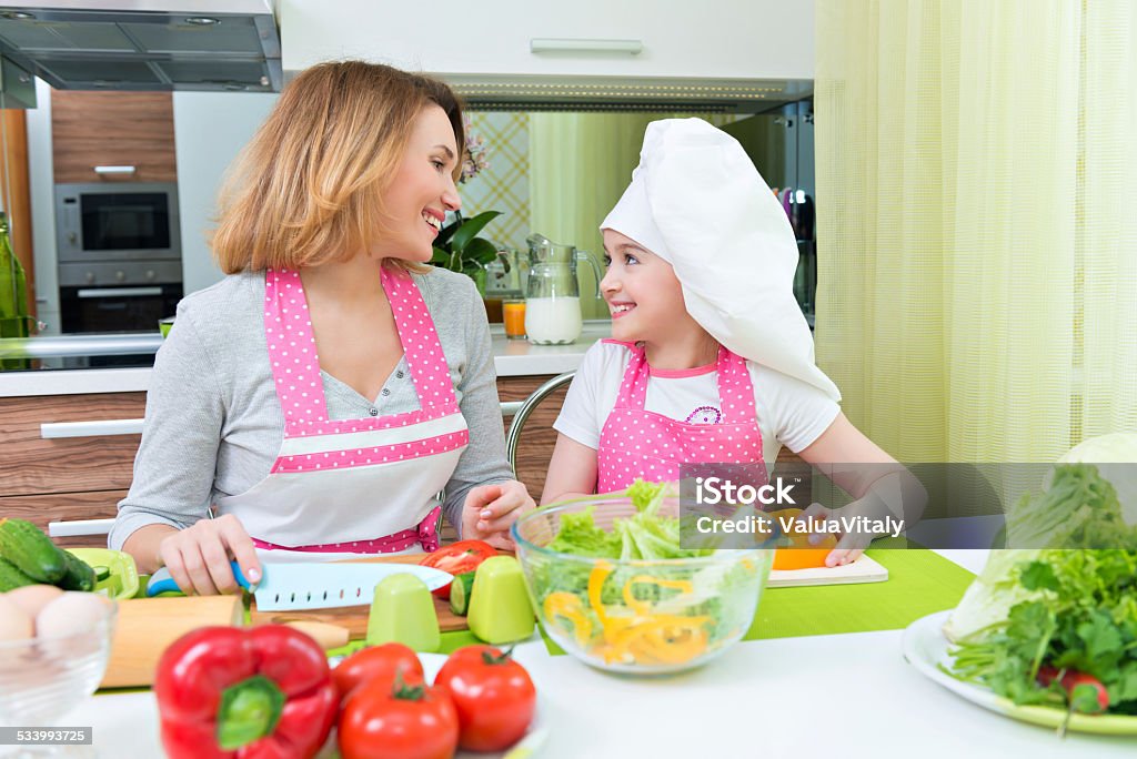 Happy mother and daughter cooking a salad. Portrait of attractive happy mother and daughter cooking a salad at the kitchen. 2015 Stock Photo