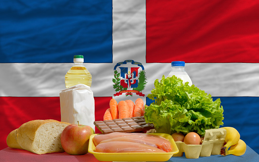 complete national flag of dominican covers whole frame, waved, crunched and very natural looking. In front plan are fundamental food ingredients for consumers, symbolizing consumerism an human needs