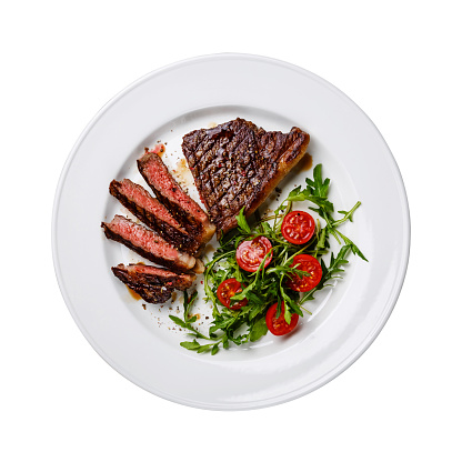 Sliced medium rare grilled Beef steak Striploin and salad with tomatoes and arugula on white plate isolated