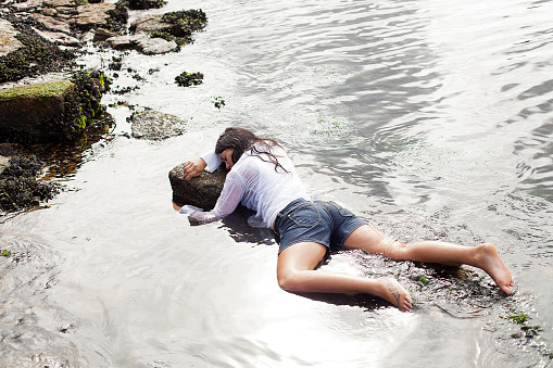 View of a young woman washed up on rocks at the edge of a river, possible boating accident victim
