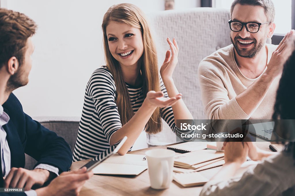 Sharing the latest news. Cheerful young people looking at each other with smile while sitting at the office table at the business meeting Meeting Stock Photo