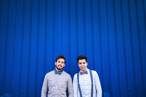 Portrait of young gay couple on blue .