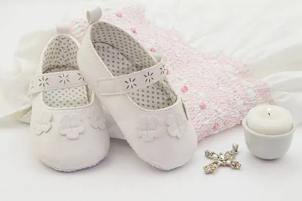 Photo of Pair of white baby shoes on embroidered christening white dress,
