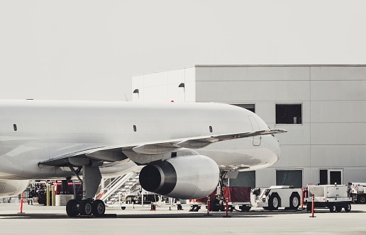 A cargo jet sits on the tarmac while being loaded from a nearby warehouse.