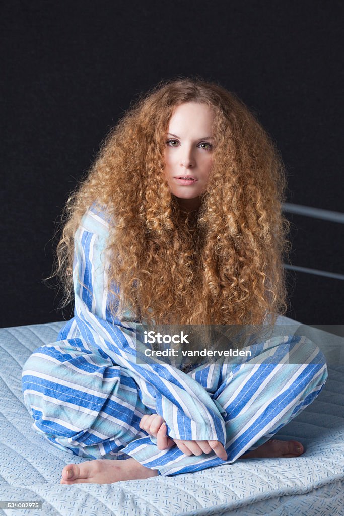 Blond Wearing Traditional Mens Pyjamas Cute girl with long, frizzy, blond hair, sitting cross-legged on a mattress in Men's old-fashioned, stripey pyjamas. 20-29 Years Stock Photo