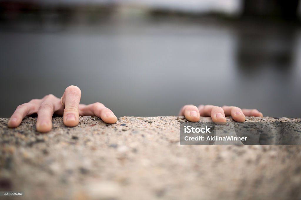 Hands of a woman holding on edge of the wall. Hands of a woman gripping on the edge on stone wall. Wall - Building Feature Stock Photo