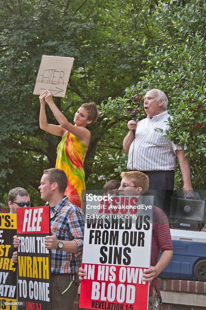 Religious Disagreement Asheville, North Carolina, USA - July 26, 2013: Up on a stage, a young woman holds a sign saying "HATER" with an arrow pointing to an older man next to her preaching Scripture as young men below hold large, colorful signs quoting Scripture at the 2013 Bele Chere Festival in Asheville, North Carolina 2015 Stock Photo