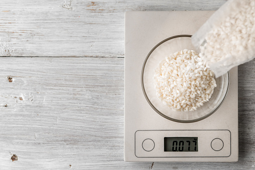 Rice in the glass bowl on the scale on the white table top view