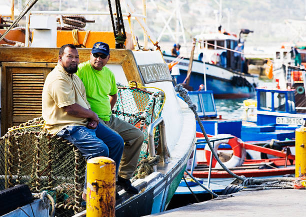 Cape Town, South Africa - September 18, 2007: Fishermen relax between sea trips as they sit on their boat in the fishing harbour at Kalk Bay on the False Bay coast near Cape Town. The harbour is noted both for its restaurants, catering to locals and tourists, and real working fishing vessels that continue a tradition dating back centuries.