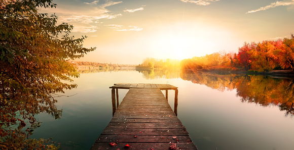 Red autumn and wooden fishing pier on river