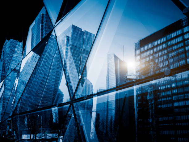 View of a modern glass skyscraper reflecting the buildings around View of a modern glass skyscraper reflecting the blue sky,blue toned image. office block exterior stock pictures, royalty-free photos & images