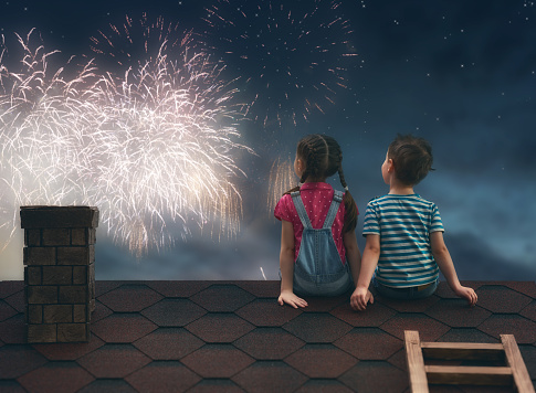 Two cute children sit on the roof and look at the fireworks.