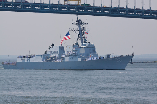 New York, NY, USA - May 25, 2016: NYC Fleet Week 2016, USS Bainbridge (DDG 96) guided missile destroyer entering New York Harbor under Verrazano-Narrows Bridge. US Navy sailors are lined up on the ship's deck under US flag. Fleet Week has held since 1984 to honor the U.S. Navy and Marine Corps. Image taken in the morning. 