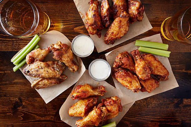 overhead view of four different flavored chicken wings with beer overhead view of four different flavored chicken wings with ranch dressing, beer, and celery sticks appetizer stock pictures, royalty-free photos & images