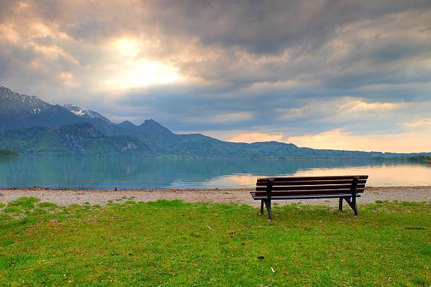 Empty bench at spring montain lake. The coast with mountains at horizon and in water mirror. Vintage toned photo.