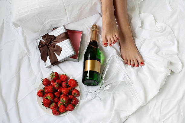 beautiful woman legs in bed romantic morning gift strawberry champagne Top view