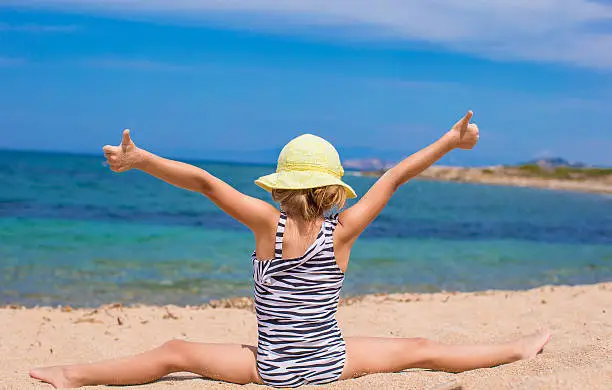 Cute little girl having fun making leg-split and enjoying vacation on tropical beach