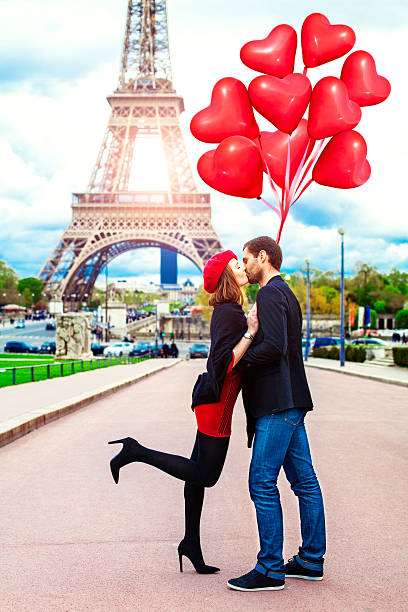 Young romantic couple kissing near the Eiffel Tower in Paris Young romantic couple kissing near the Eiffel Tower in Paris and  holding red heart shape balloons.  Image taken during istockalypse Paris 2016 paris france eiffel tower love kissing stock pictures, royalty-free photos & images