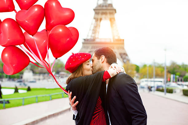 Young romantic couple kissing near the Eiffel Tower in Paris Young romantic couple kissing near the Eiffel Tower in Paris and  holding red heart shape balloons.  Image taken during istockalypse Paris 2016 paris france eiffel tower love kissing stock pictures, royalty-free photos & images