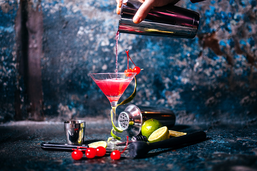 barman preparing and pouring red cocktail in martini glass. cosmopolitan cocktail on metal background