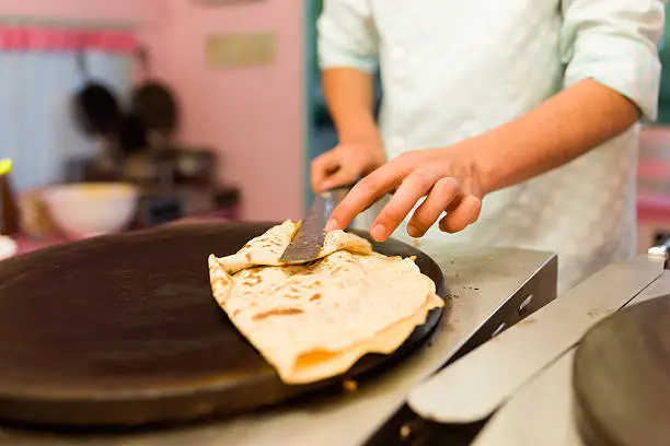 Close-up of young man cooking crepes with chocolate in a food truck.