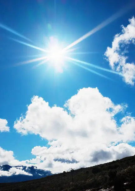 Photo of Dazzling noonday sun radiating in bright blue, lightly clouded sky