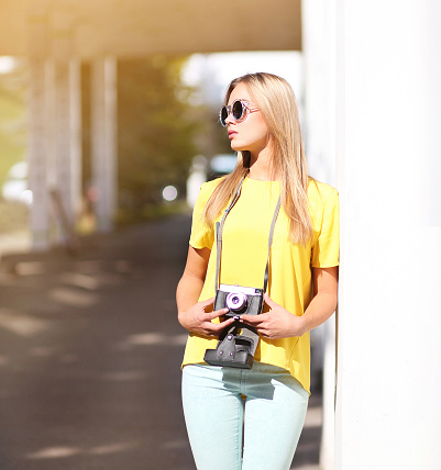 Stylish hipster cool girl in sunglasses with retro vintage camera outdoors, street fashion
