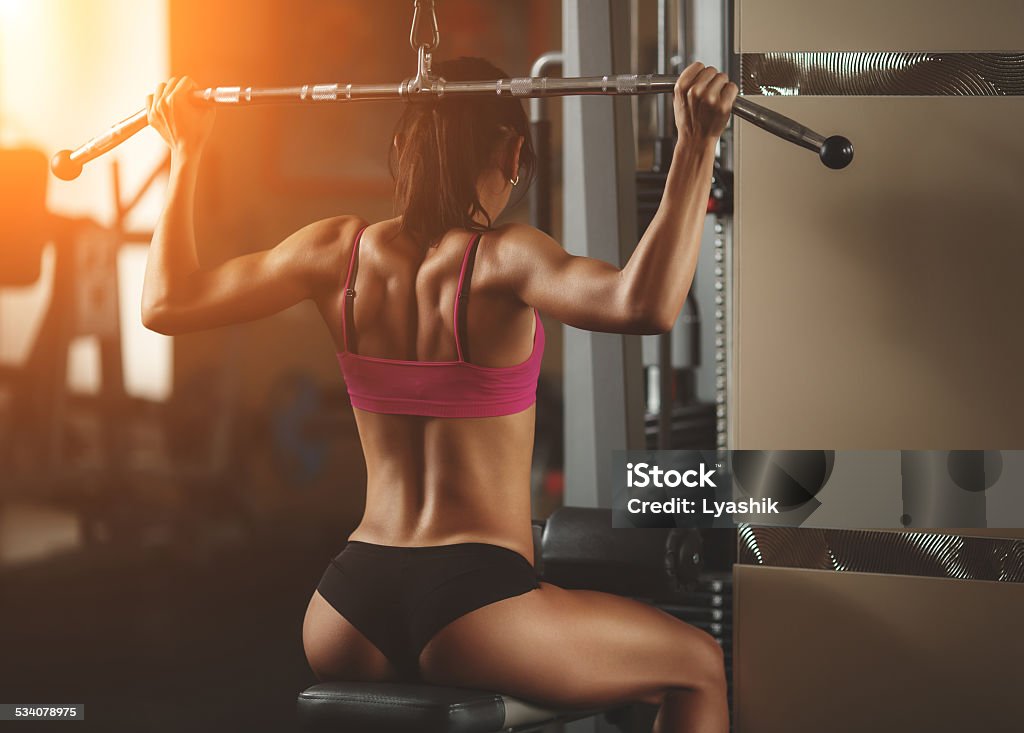 Brutal athletic woman pumping up muscles with dumbbells Brutal athletic woman pumping up muscles with dumbbells. Brunette sexy fitness girl in pink sport wear with perfect body in the gym posing before training set. Attractive fitness woman 2015 Stock Photo