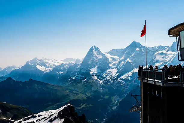 The observation deck and restaurant at the top of the Schilthorn in the Bernese Alps, Switzerland. Tourists can be seen on the observation deck. The Jungfrau, Monch and Eiger mountains can be seen in the background.