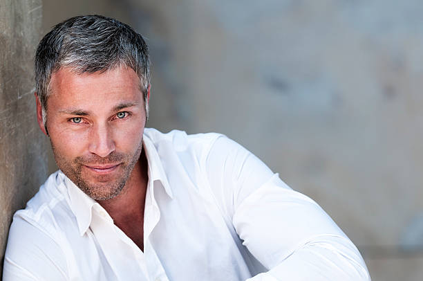 attractive businessman with grey hair leaning at a wall smiling at camera