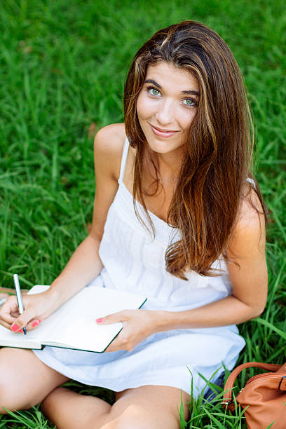 Happy woman writing on notebook lying on grass on a park