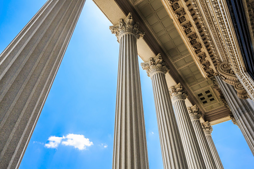 Majestic columns frame blue sky and puffy white clouds.Bright sun flare at top of picture.