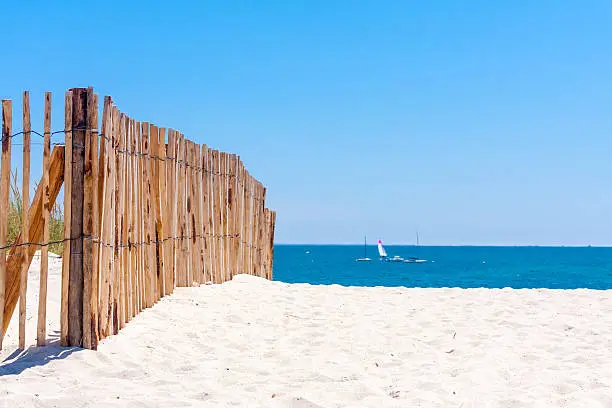 A wooden fence on a white sandy beach on a sunny day with clear blue sky