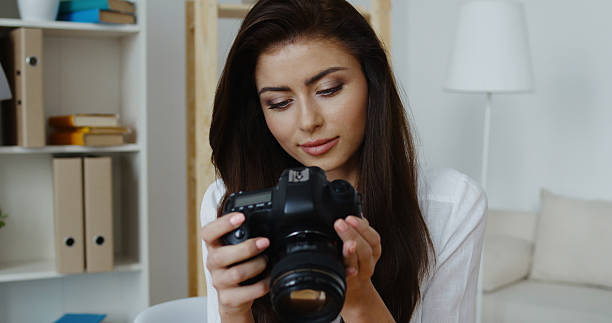 istock Cute young smiling brunette wearing white shirt sitting holding camera 534112818