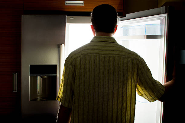 Bachelor Looking For Food in a Fridge Man looking for food in an open fridge in a dark kitchen late at night.  The man looks like a bachelor.  He is hungry and starving so he is looking for a snack.  The kitchen is dark like it is night time. bachelor stock pictures, royalty-free photos & images