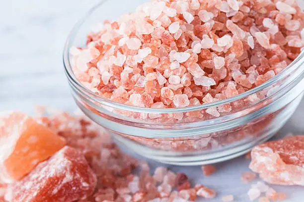 Natural light photo of bowl of Himalayan Pink Salt in with small and large chunks. Selective focus on top of salt in bowl