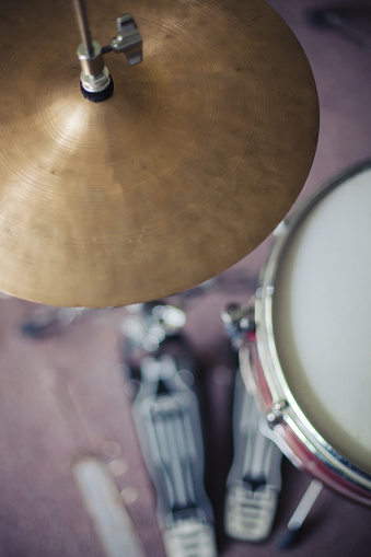 Close up image with focus on high hat cymbals and blurred red drum kit in the background, shot from above looking down. Focus on high hat with snare drum and sticks slightly blurred.