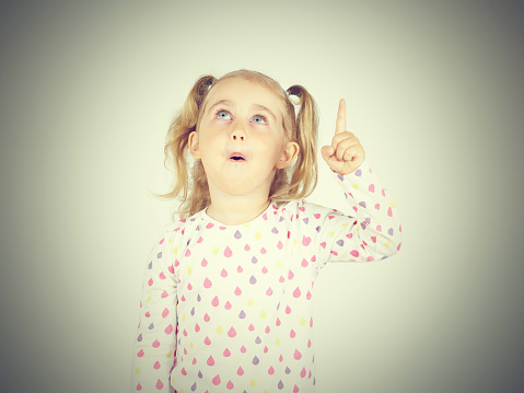 little girl wearing  pointing by forefinger to somewhere up isolated